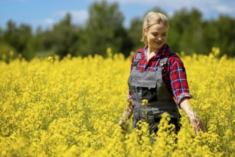 A cheerful woman dressed in denim overalls joyfully explores a vibrant yellow flower field beneath