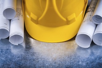 Metallic background with white architectural blueprint rolls and yellow building helmet close up