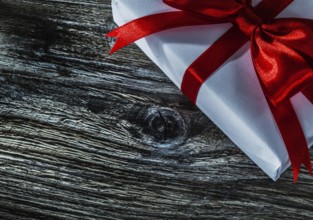 White gift box with red bow on wooden board
