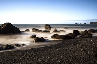 Rocks by the sea with foaming waves under a clear blue sky, Iceland, Europe