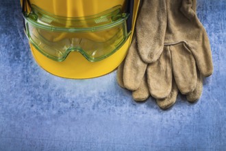 Safety leather gloves hard hat and multiple-purpose protective glasses on scratched metallic