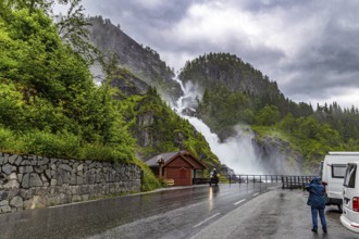 Woman tourist taking pictures of scenic double waterfall Lotefossen. Summer rainy day. The road