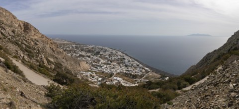 View down to serpentine road and Kamari at the lava beach, in the sea the island Anafi, panoramic