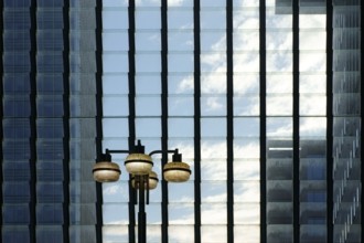 A glass façade with rows of hinged windows in front of which a lantern stands and tower blocks
