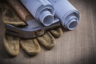 Rolled blueprints protective gloves and claw hammer on wooden board