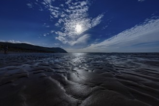Dimly lit beach with dramatic sky and sparkling sea on the edge of Snowdonia National Park,