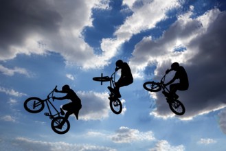 An extreme rider is making a free style jump from a ramp. The young boy with his bicycle is seen as