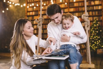 Family With Baby Relaxing On home Swing Seat in cozy dark living room on Christmas eve. Family