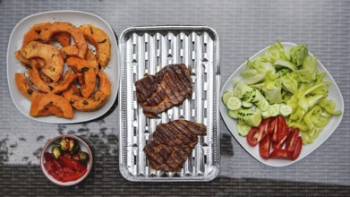 Grilled butternut squash and pork cuts, some fresh vegetable next to it, on glass garden table,