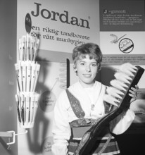 A young woman from the company Jordan is standing in their booth at an exhibition, holding a giant