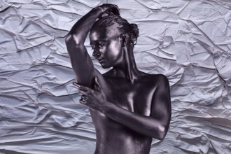 Young beautiful naked woman with glossy skin is posing on the crumpled paper background