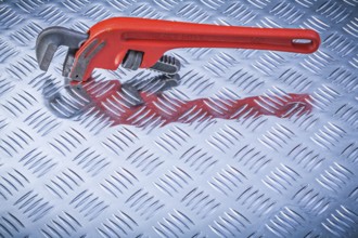Metal pipe wrench on corrugated metallic background directly above maintenance concept
