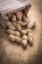 Peanuts poured from paper bag on wooden board food and drink still life