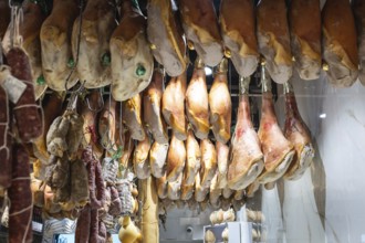 Large hams and other cold cuts hanging in an Italian shop