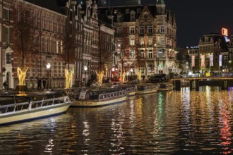 A night-time view of the canal with illuminated boats and imposing buildings, Amsterdam,