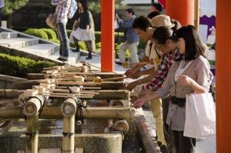 People washing hands at a Tsukubai in front of the Inari Shrine in Kyoto in order to purify