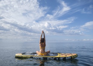 Woman practicing yoga on a surfboard under a dramatic sky, Estalella, coast of Llucmajor, Majorca,