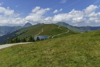 Hilly mountain landscape with hiking trail and small lake under a blue sky, mittersill, hohe