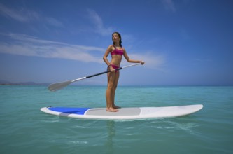 Girl standing on paddle surf board SUP in summer