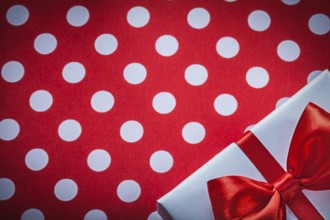 White present box with knot on polka-dot red fabric holidays concept