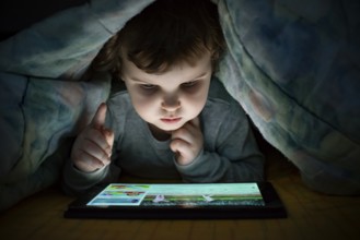 Little girl watching her tablet in the bed. Illuminated child face from device screen. Child