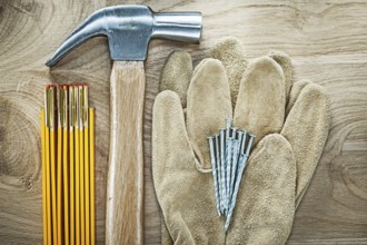 Pair of safety gloves wooden meter claw hammer nails on wood board construction concept