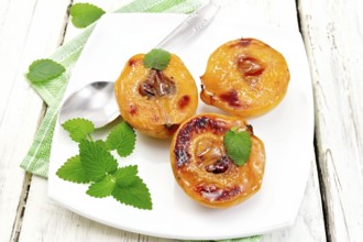 Three halves of quince baked with honey, mint and spoon in a plate on a napkin against a light