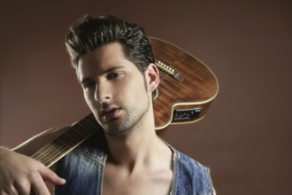 Handsome sexy young man musician guitar player portrait on brown