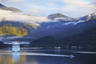 Snow-white tourist boat lit rising sun. On the mountains are thin clouds. Sunrise in the Chilean