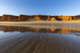 A landscape on the beach at low tide. The surrounding rocks and cliffs are reflected in the sea at