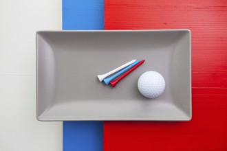 Gray ceramic dish with golf equipments on over white, blue and red wooden table, rectangle dish