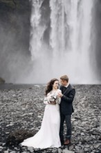 Wedding couple near Skogafoss waterfall. Destination Iceland wedding. The groom hugs the bride by