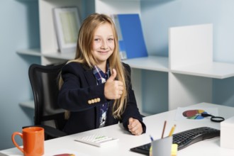 Little girl like business woman sitting at the desk with computer in blue office