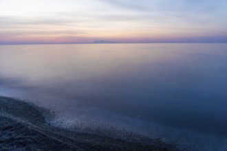 Dawn, cloudy mood in front of sunrise, view from the lava beach to the island of Anafi, long