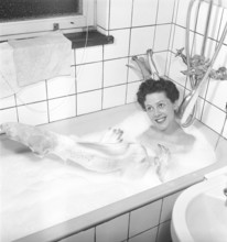 Having a bath 1950. A young smiling woman wearing a princess crown, is having a bath in a bathtub