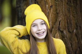 Portrait of modern happy teenage girl with braces dressed in yellow clothes in park. Pretty teenage