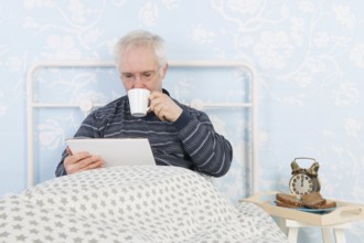 Man reading on digital tablet white having breakfast in bed