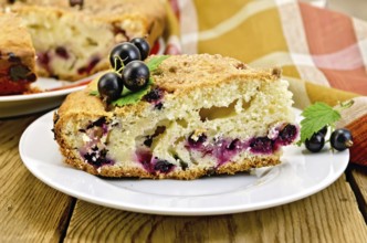 Sweet piece of cake with black currant on a plate, napkin on the background of wooden boards