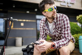 Individual urban environmental friendly transport electric kick scooter parked near man sitting on