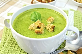 Green soup puree in a white bowl with croutons and spinach leaves on a napkin on the background