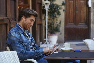 Young man with tablet pc touch in an cafe outdoor having some coffe cup