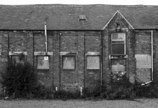 An old abandoned brick factory building with boarded up windows and crumbling decaying walls