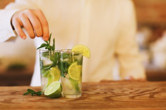 Bartender making two mojito cocktails on wooden bar counter