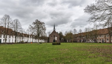 Belgium, 12 08 2018: Old houses and a chapel at the beguinage with bare trees and a meadow during