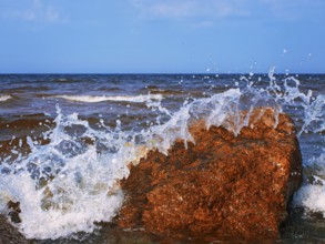 Water splashes over the red rocks against blue sky