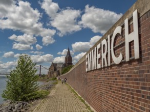 Brick wall and sign of Emmerich, next to it a path along the river on a sunny day, emmerich, lower