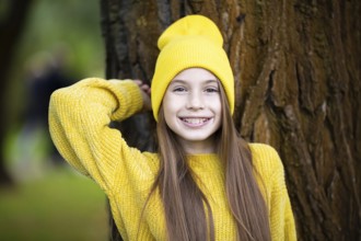 Cute and happy teenage girl with braces smiling at camera in yellow clothes in park. Concept of