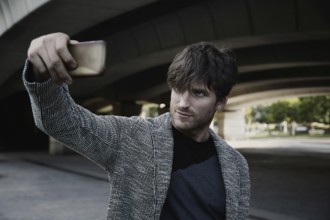 Modern young man smartphone taking selfie photos under a bridge