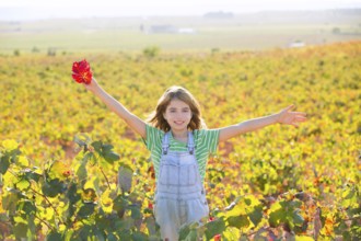 Kid girl in happy autumn vineyard field open arms with red leaf in hand