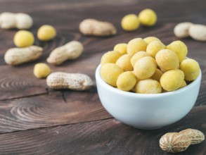 Peanut snack for beer, wine, party bar. Salted peanuts in yellow cheese glaze on brown wooden table